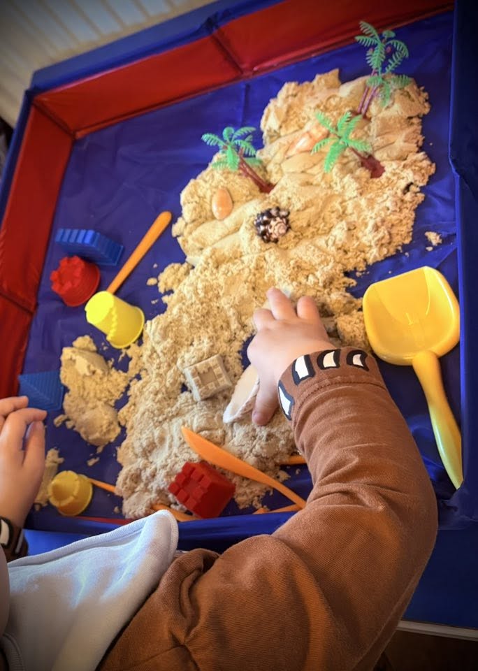 A dinosaur sensory play tray with sand and colourful tools